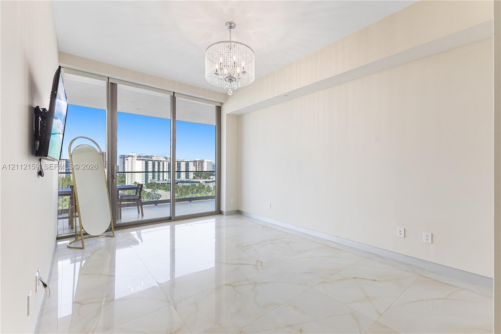 Polished large-format tile flooring, drum-style crystal chandelier, and floor-to-ceiling sliding glass doors opening to a private balcony