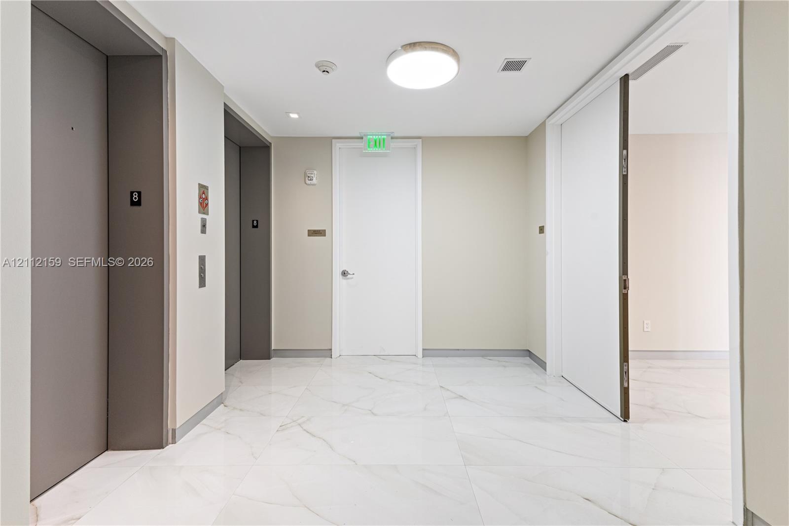 Common area featuring large-format white stone-finish tile flooring, dual elevators with metallic finishes, and recessed ceiling lighting