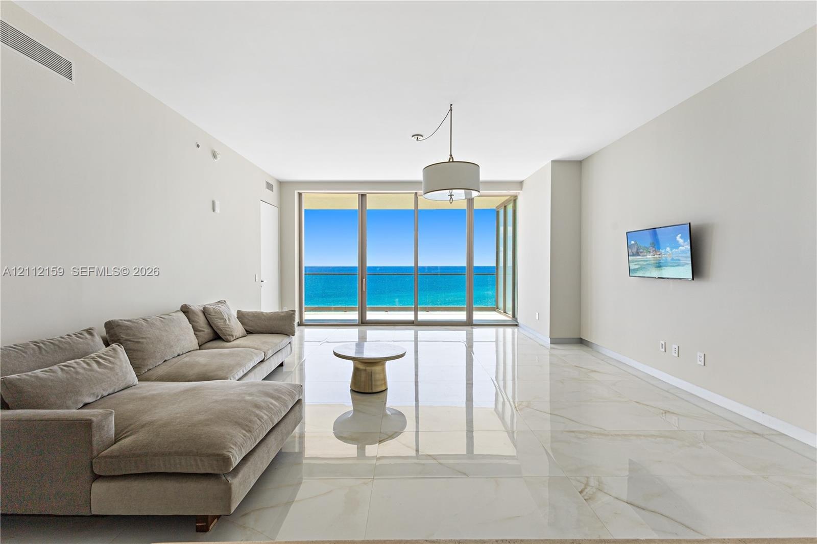 Floor-to-ceiling sliding glass doors, polished stone-finish tile flooring, recessed lighting, and a pendant fixture
