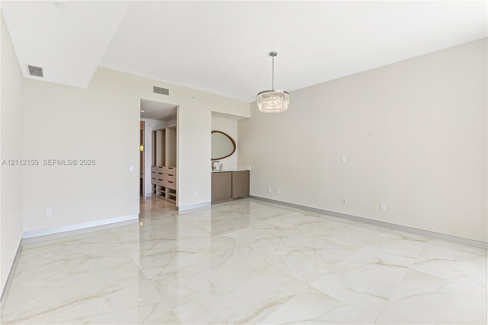 Expansive room featuring polished stone flooring, built-in cabinetry with a stone countertop, custom walk-in closet shelving, and a modern drum pendan
