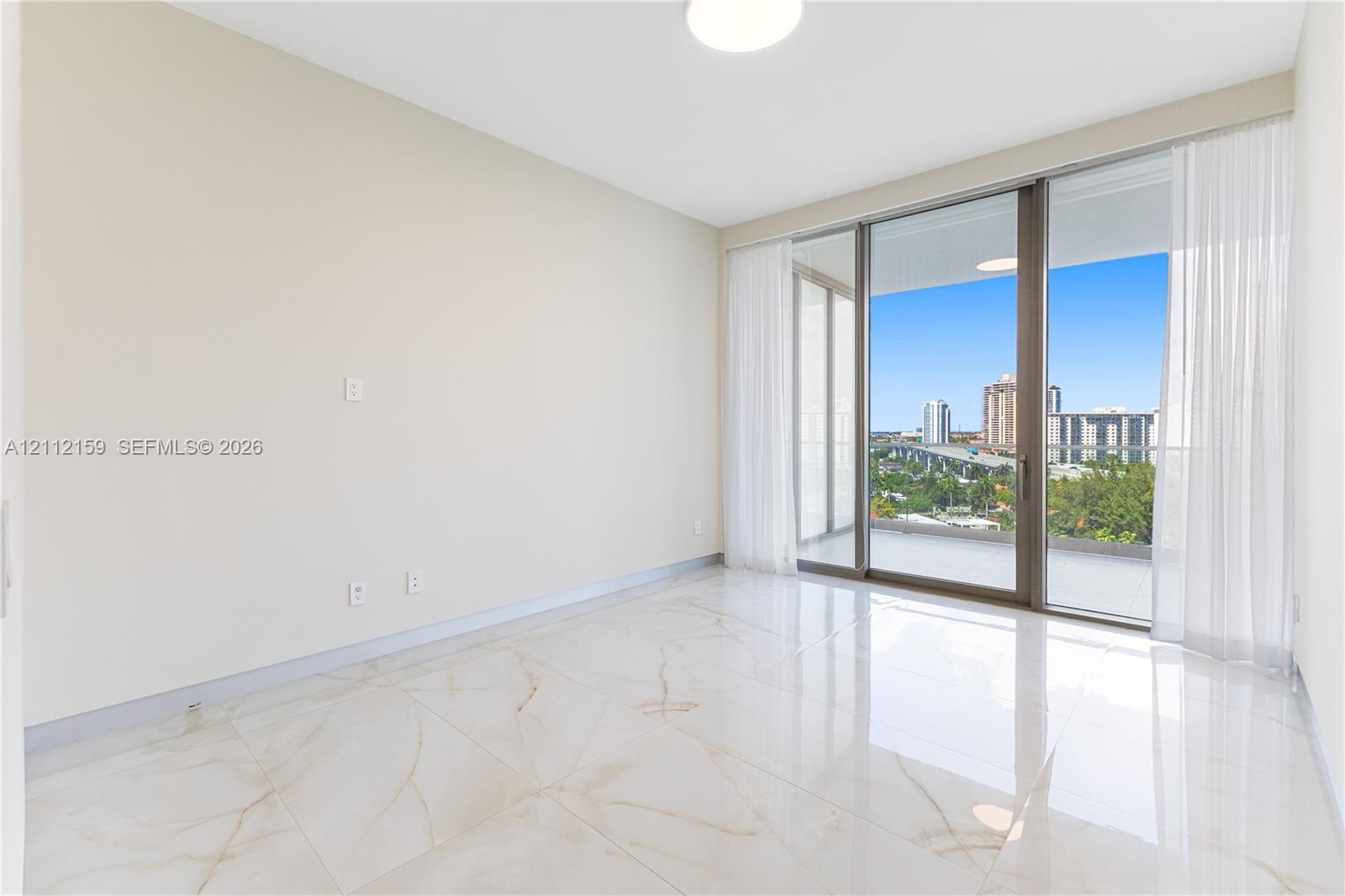 Interior space featuring large-format stone-finish floor tiling, floor-to-ceiling glass sliding doors, and access to a covered outdoor balcony