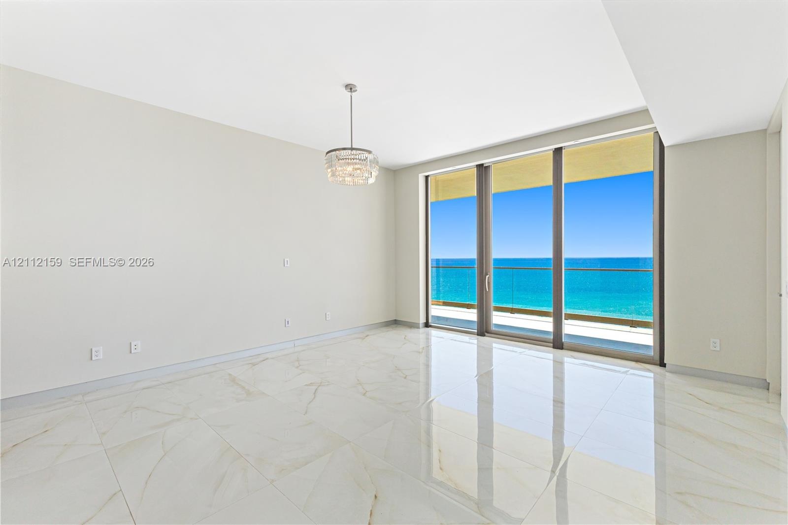 Polished stone flooring, crystal-accented chandelier, floor-to-ceiling glass sliding doors, and private balcony with ocean backdrop