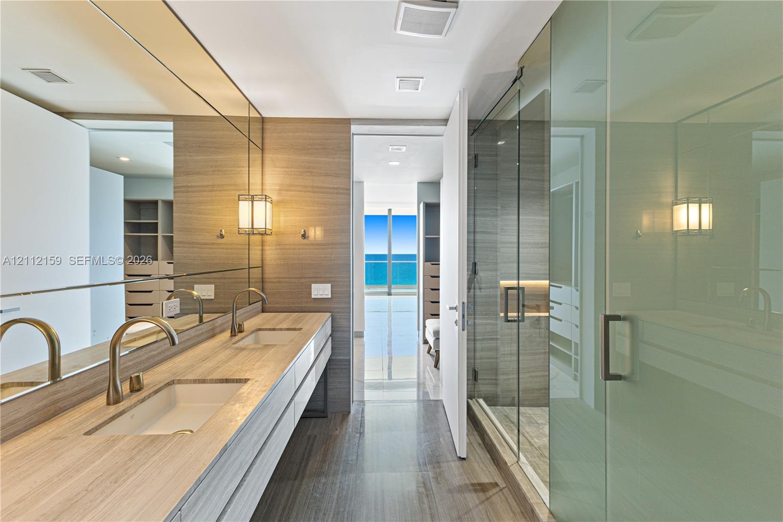 Dual vanity with wood-finish cabinetry, rectangular vessel sinks, floor-to-ceiling mirror, glass-enclosed shower, and polished stone flooring