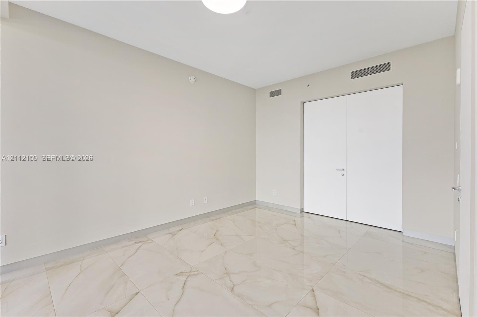 Neutral-toned room featuring large-format tile flooring with marble-pattern veining and double-door closet cabinetry