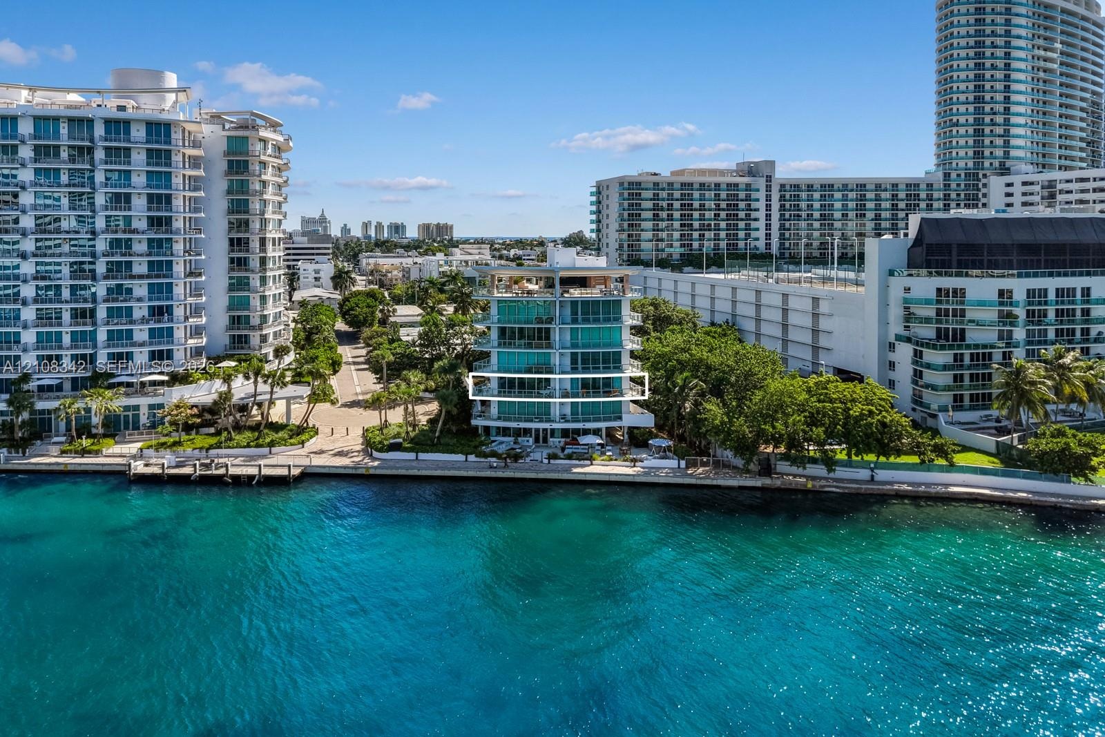 Waterfront mid-rise building featuring floor-to-ceiling glass windows, exterior balconies with glass railings, and concrete bulkhead