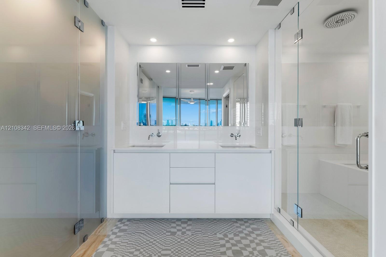 Double vanity with white cabinetry, integrated sinks, wall-mounted faucets, expansive mirrored medicine cabinet, and glass-enclosed shower with rainfa
