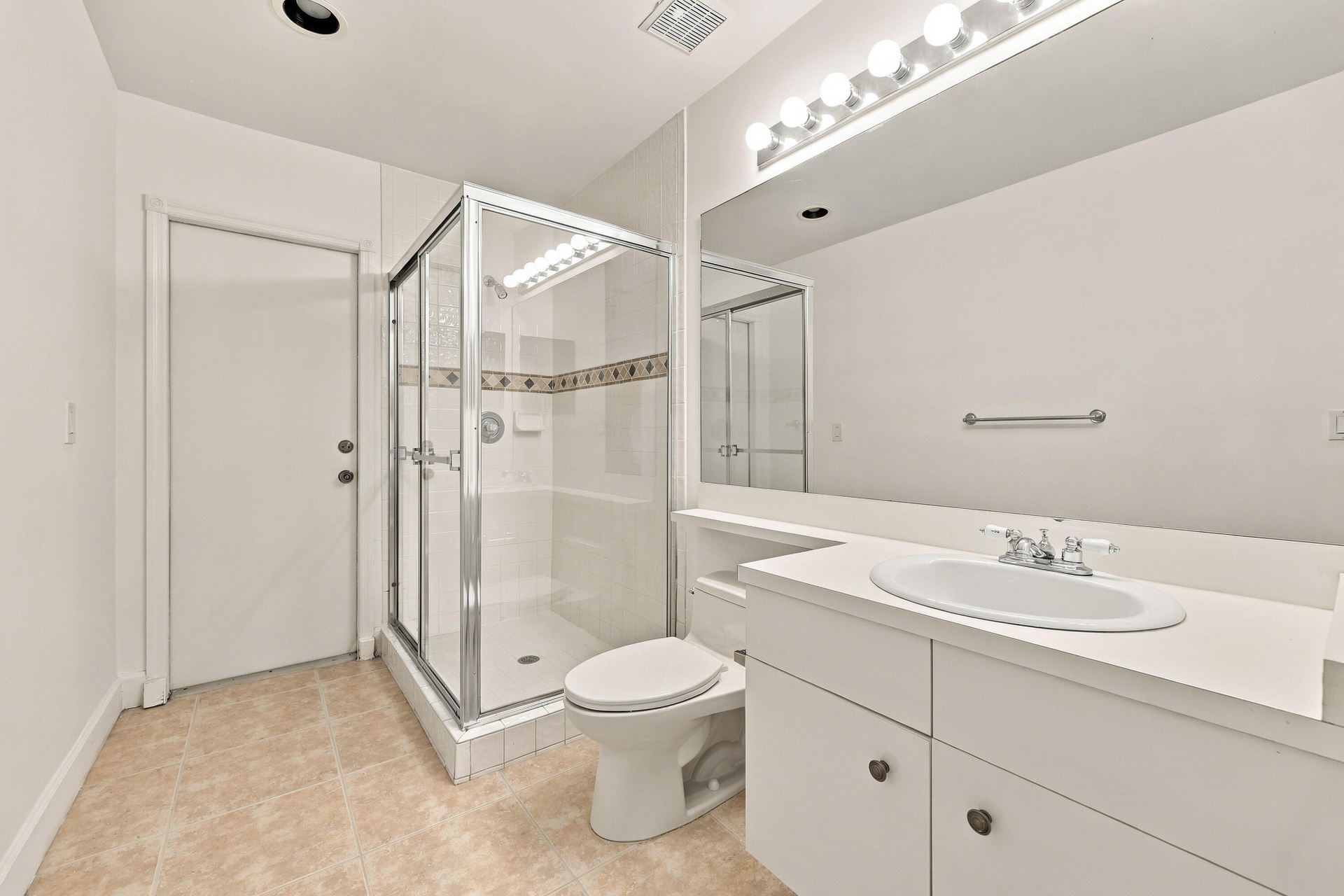This well-appointed full bathroom features a spacious vanity, large mirror, glass-enclosed shower, and convenient access from the main living areas an