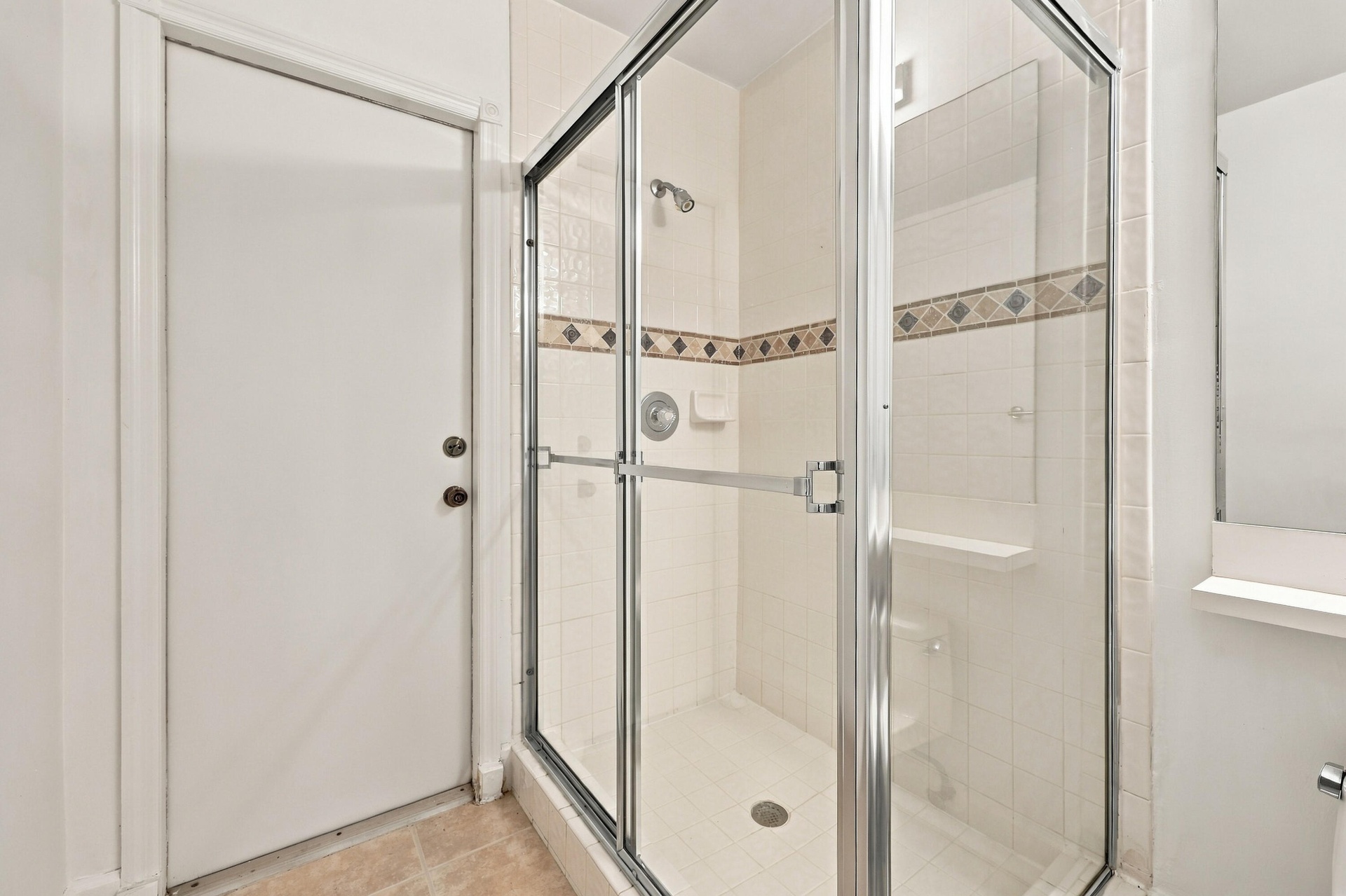 A convenient main-level guest bathroom featuring a glass-enclosed walk-in shower with decorative tile accents and neutral finishes.