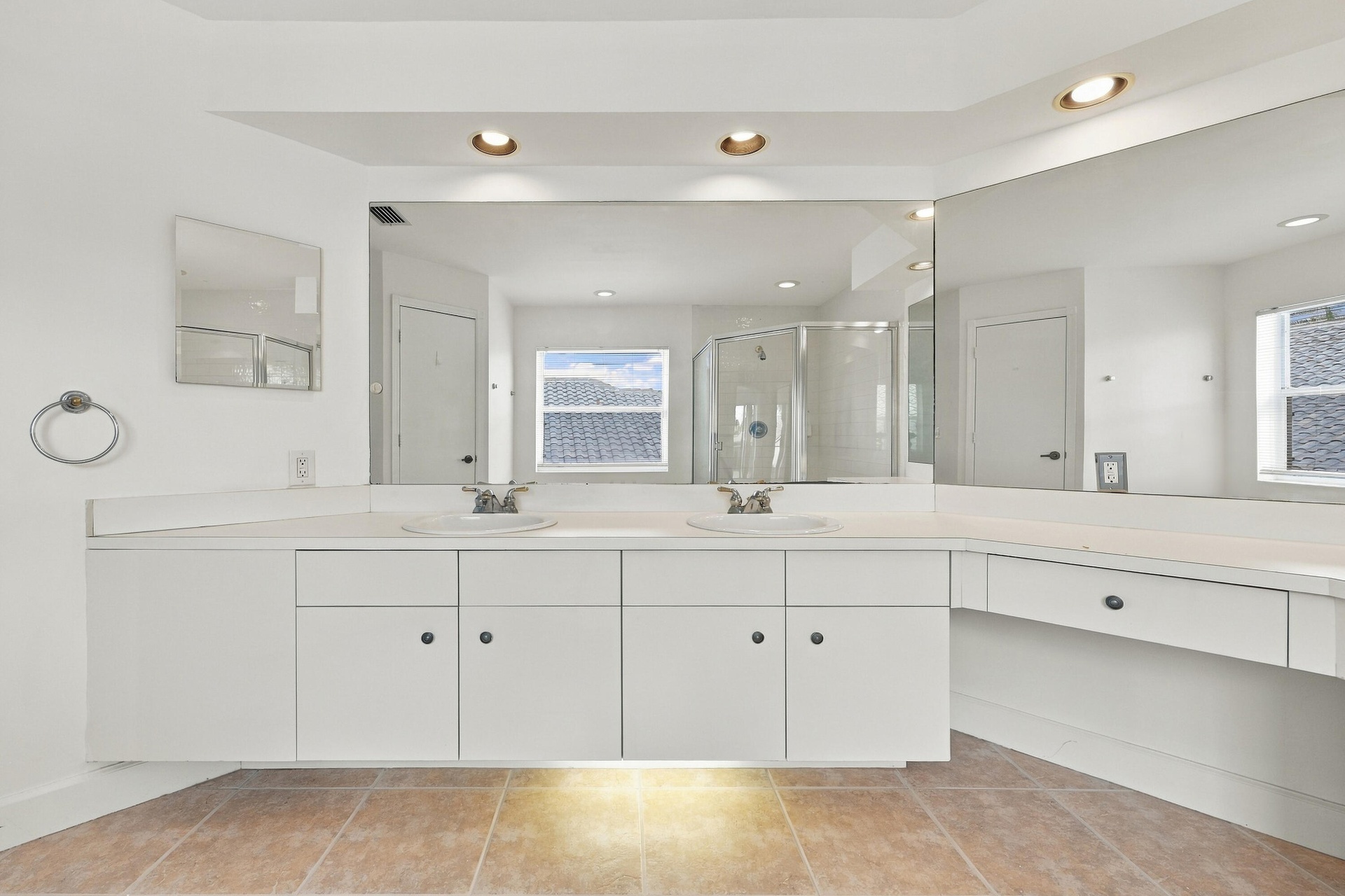 An impressive primary bathroom featuring an extended vanity with abundant cabinetry, expansive mirrors, recessed lighting, and a dedicated makeup stat