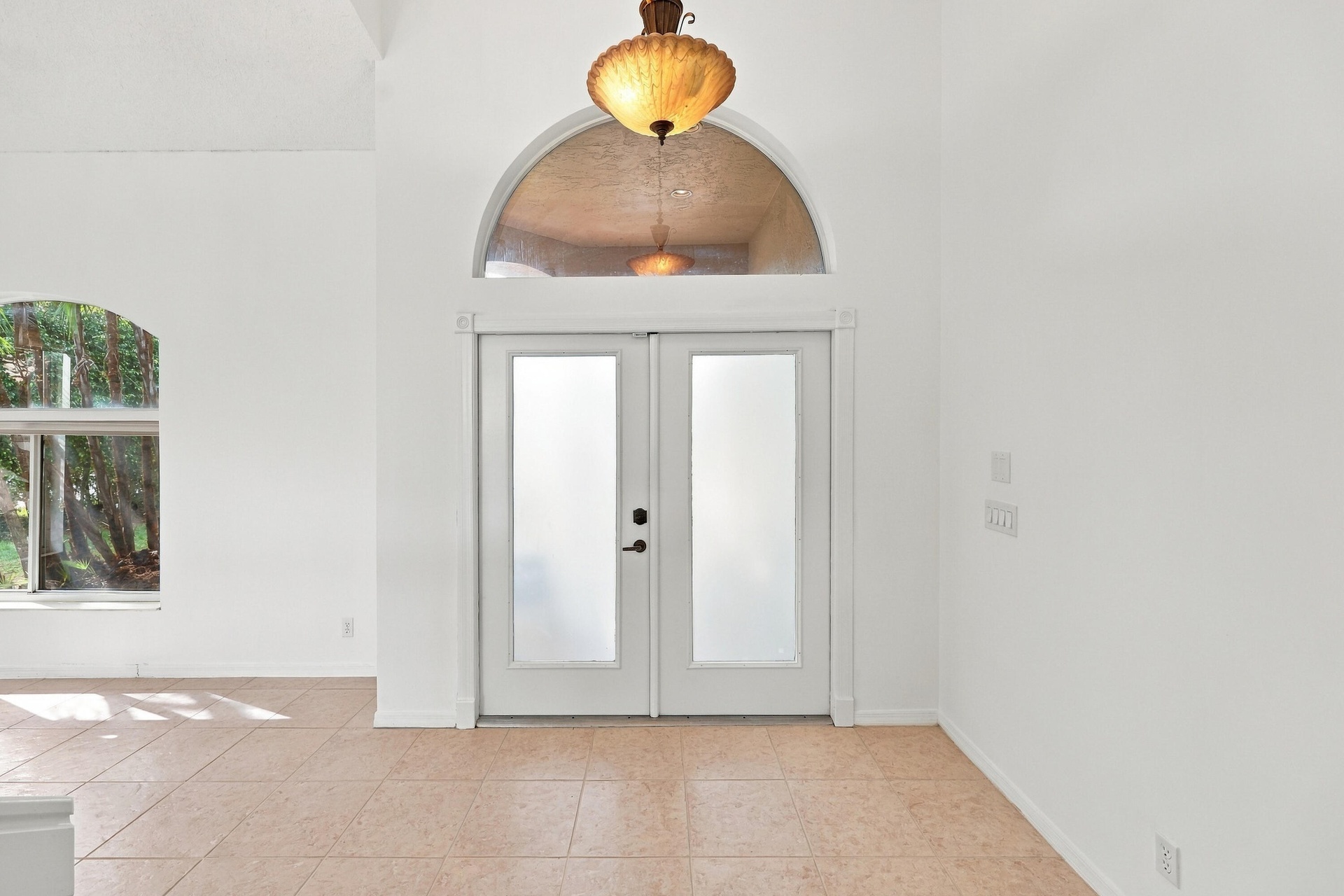 A welcoming entrance featuring elegant double doors, a decorative arched transom window, soaring ceilings, and an abundance of natural light.