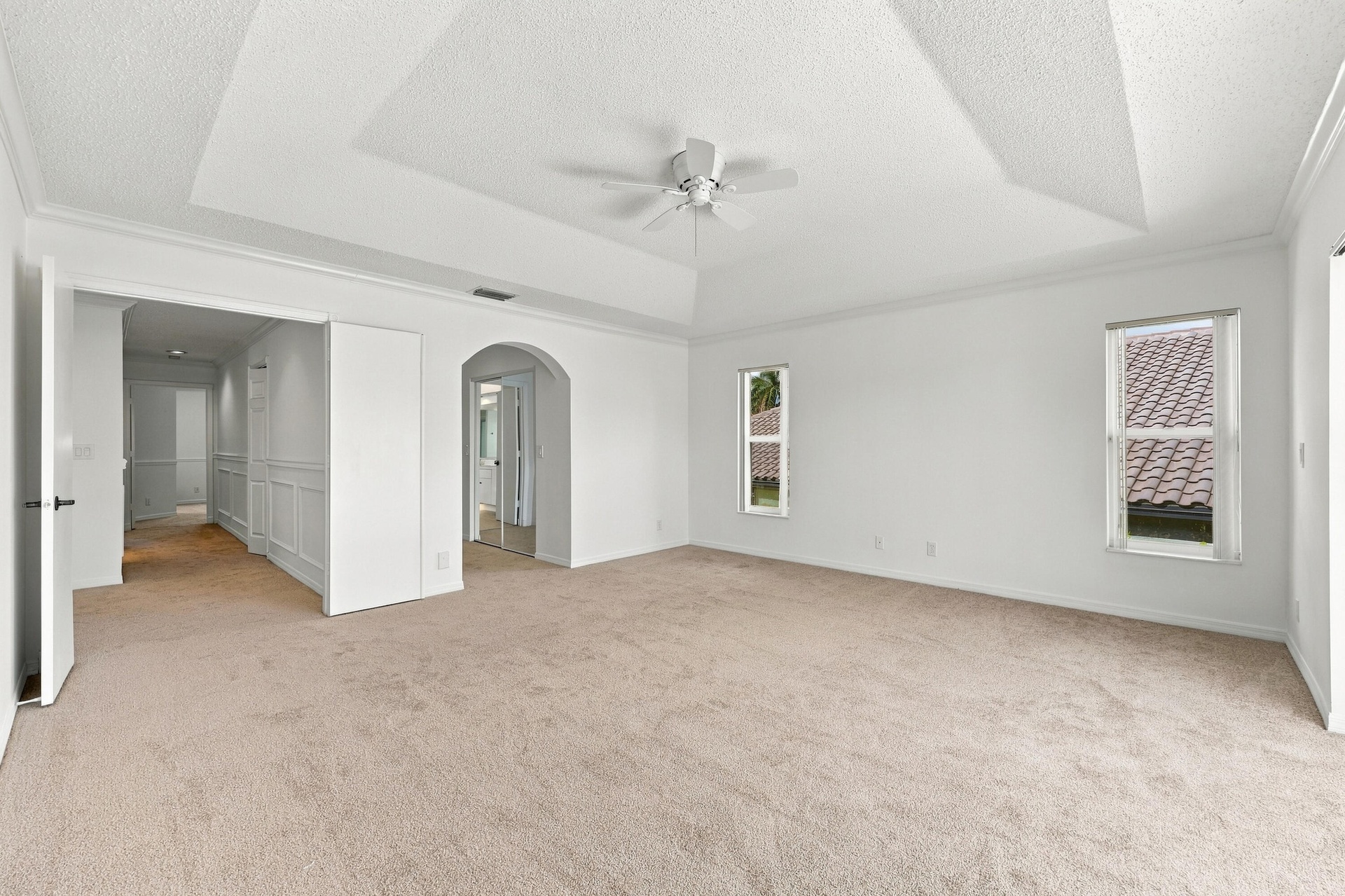 An impressive primary bedroom featuring a decorative tray ceiling, generous proportions, and a private entrance to the adjoining bathroom and dressing