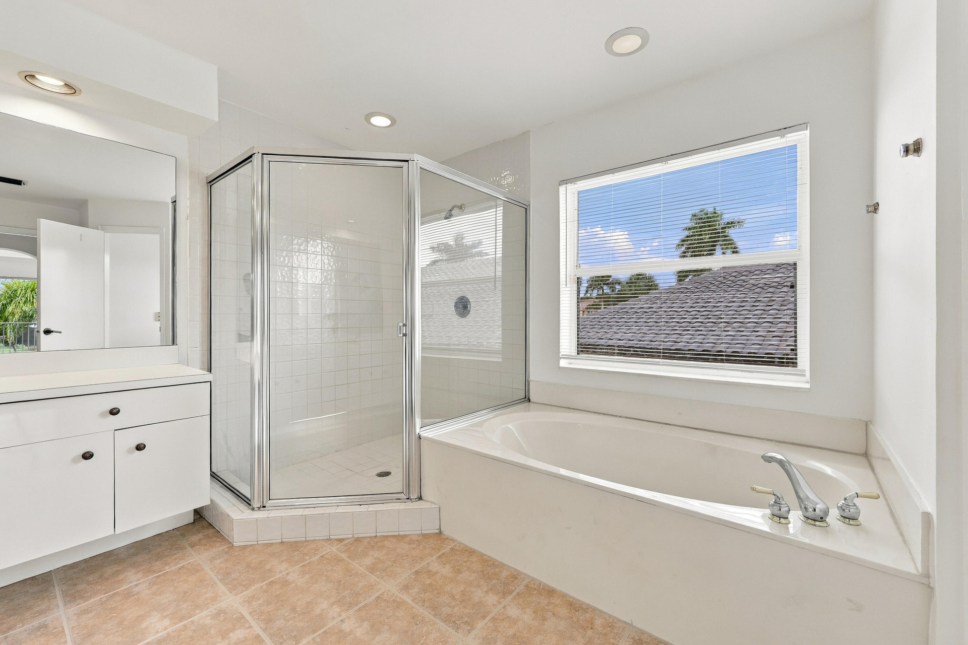A spacious primary bathroom featuring a relaxing soaking tub beneath a large window, a glass-enclosed shower, and neutral finishes that create an invi