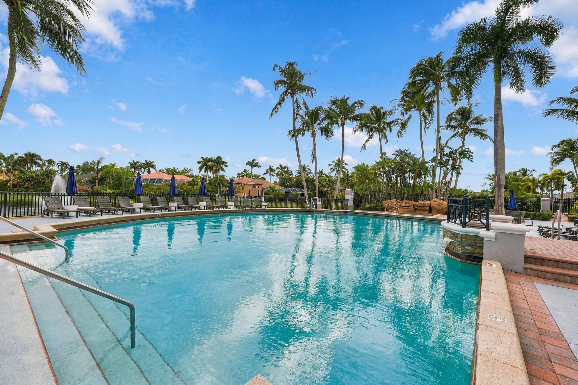 Experience resort-style living at the beautiful community swimming pool, surrounded by swaying palms, expansive lounging areas, and the impressive Boc