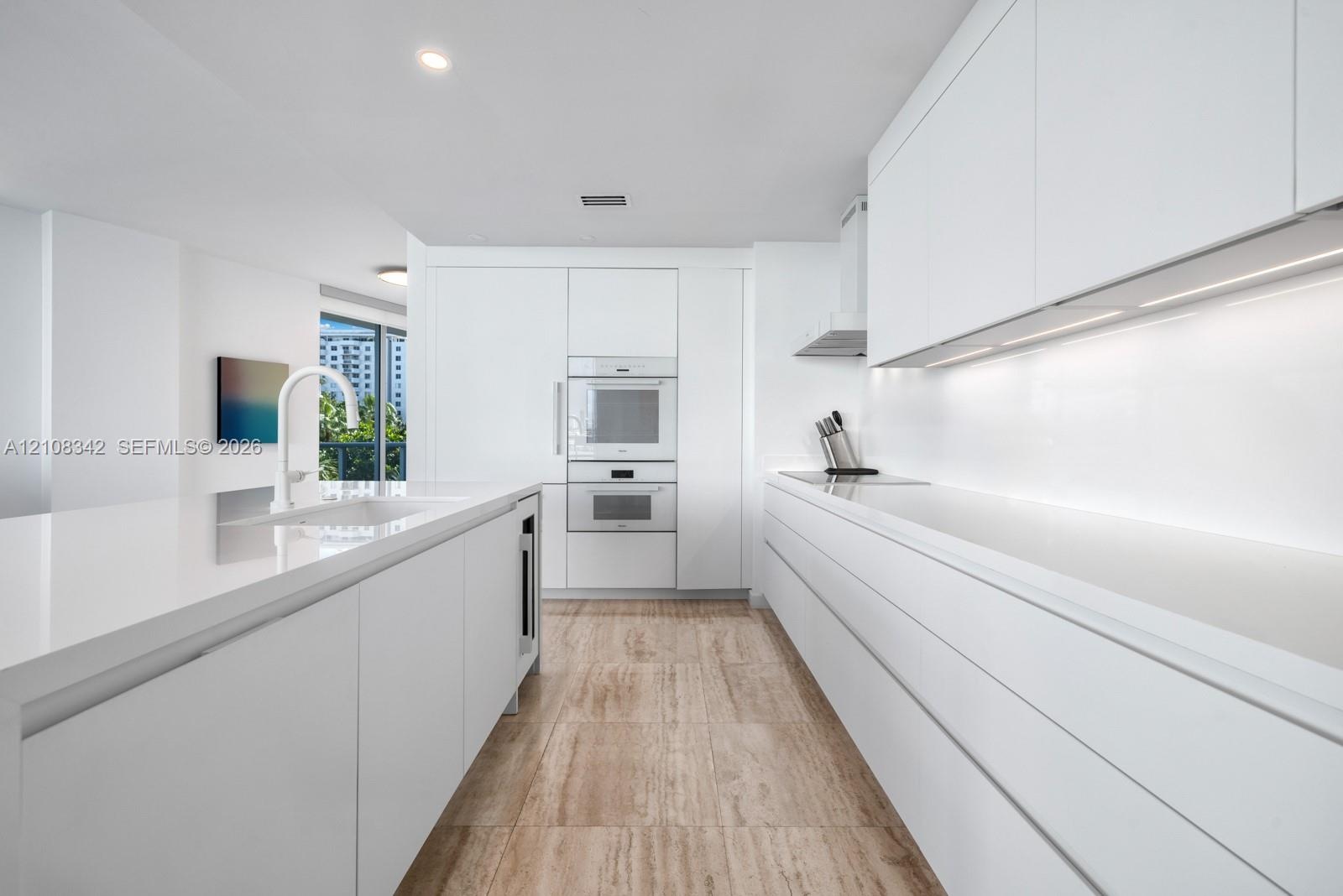 Minimalist kitchen featuring flat-panel cabinetry, white stone-surface countertops, built-in wall ovens, stone-finish flooring, and recessed ceiling l
