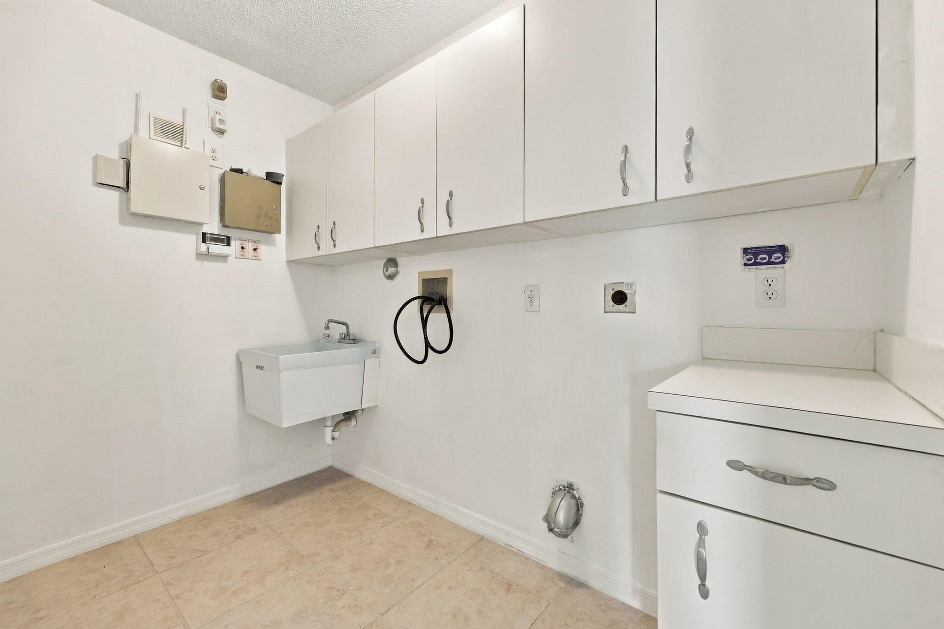 Conveniently located on the first floor, this dedicated laundry room features abundant overhead cabinetry, a utility sink, neutral tile flooring, and 