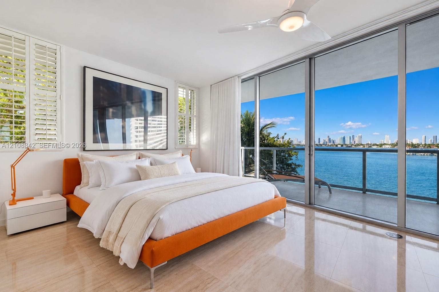 Floor-to-ceiling sliding glass doors, private balcony with metal railing, polished stone flooring, custom plantation shutters, and ceiling fan with in