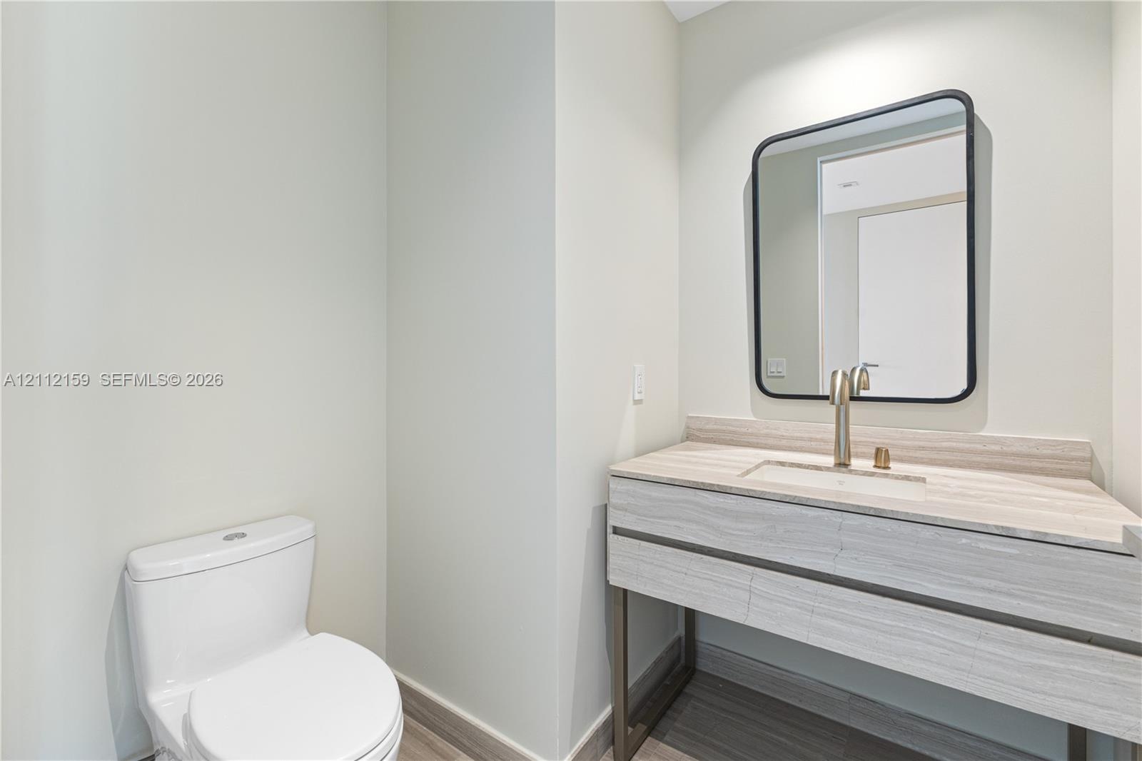 Modern vanity featuring a stone-finish countertop, integrated sink, metal-frame base, rounded rectangular mirror, and brushed-finish faucet