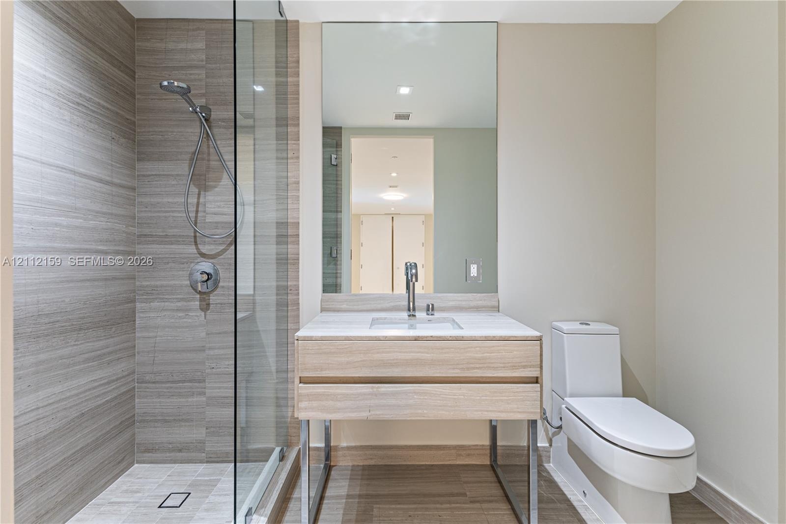 Modern bathroom featuring a wood-finish floating vanity with a light stone countertop, a glass-enclosed shower with horizontal-patterned wall tile, an