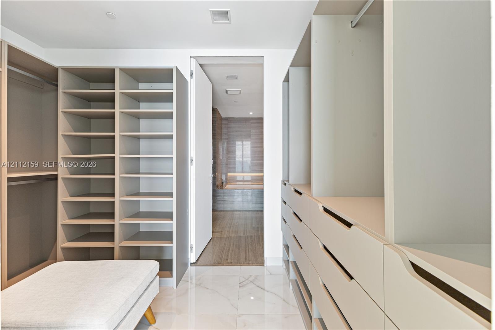 Walk-in closet featuring extensive built-in cabinetry, floor-to-ceiling shelving, recessed drawer units, and polished stone-finish flooring