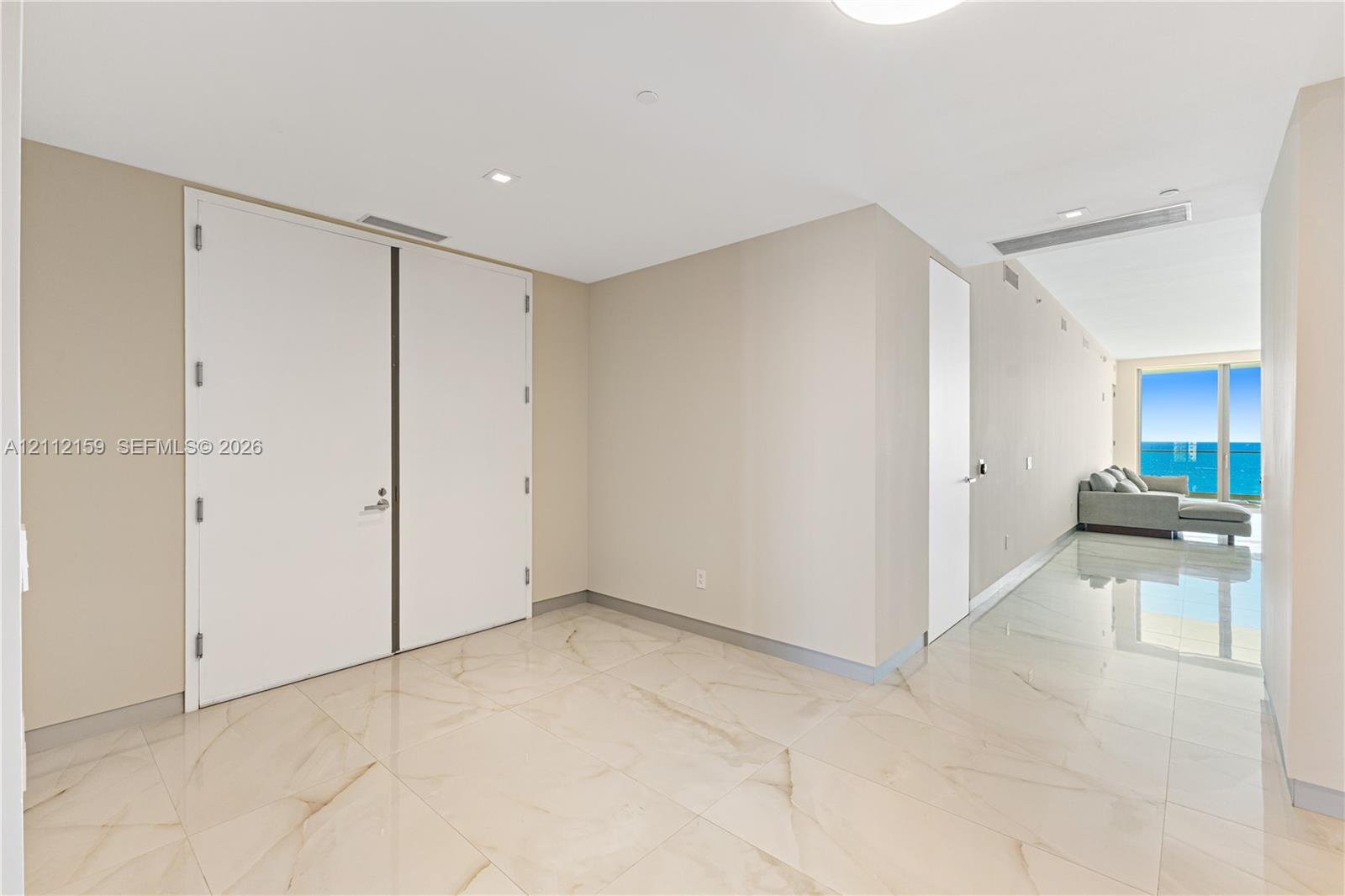 Large-format polished tile flooring with natural stone-style veining, high ceilings with recessed lighting, and expansive floor-to-ceiling windows fea