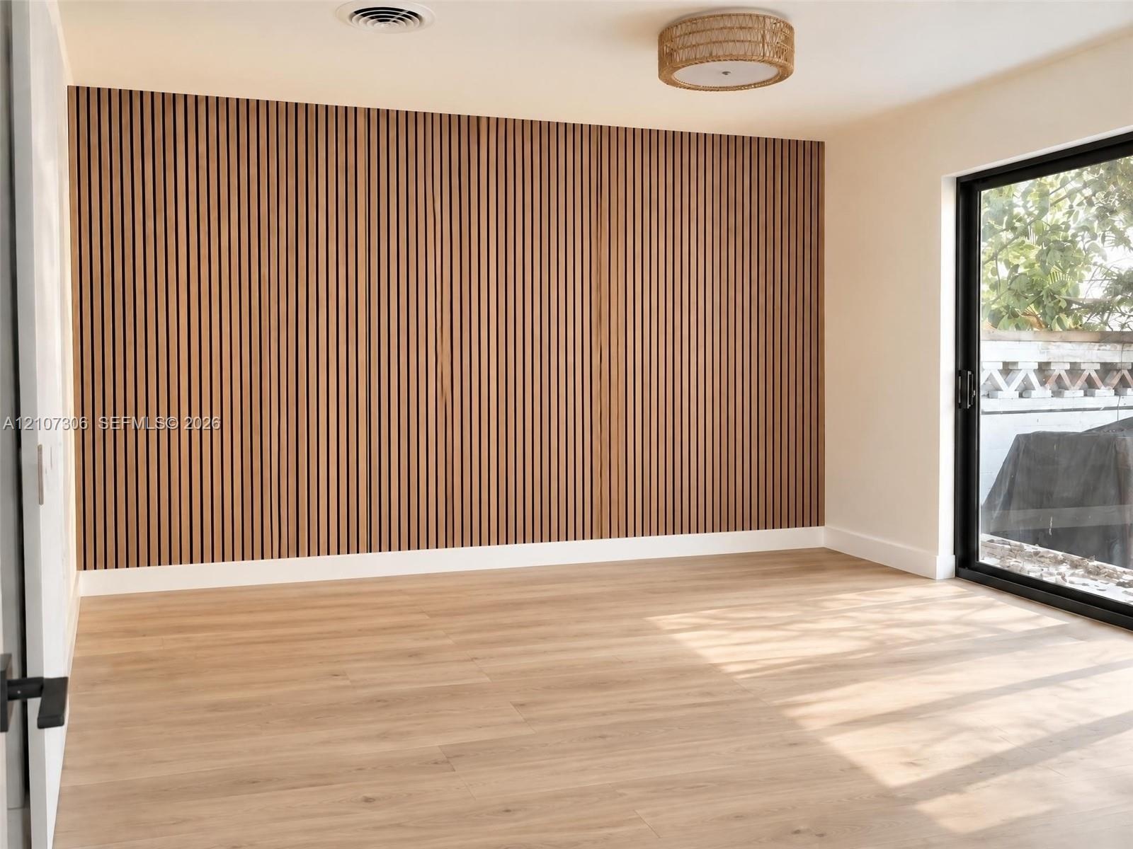 Vertical wood slat accent wall, light-toned wood-finish flooring, sliding glass door, and integrated circular drum lighting fixture