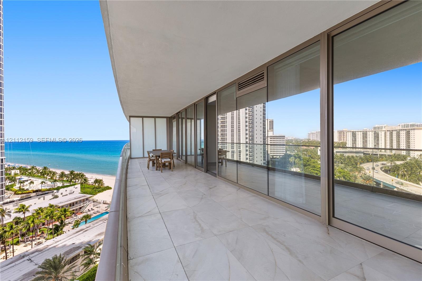 Expansive covered balcony featuring large-format tile flooring, floor-to-ceiling glass paneling, and metallic framing