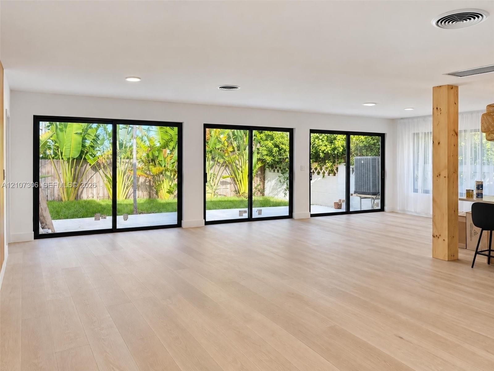Interior space featuring three sets of black-framed sliding glass doors, light-toned wood-finish flooring, recessed ceiling lighting, and an exposed s