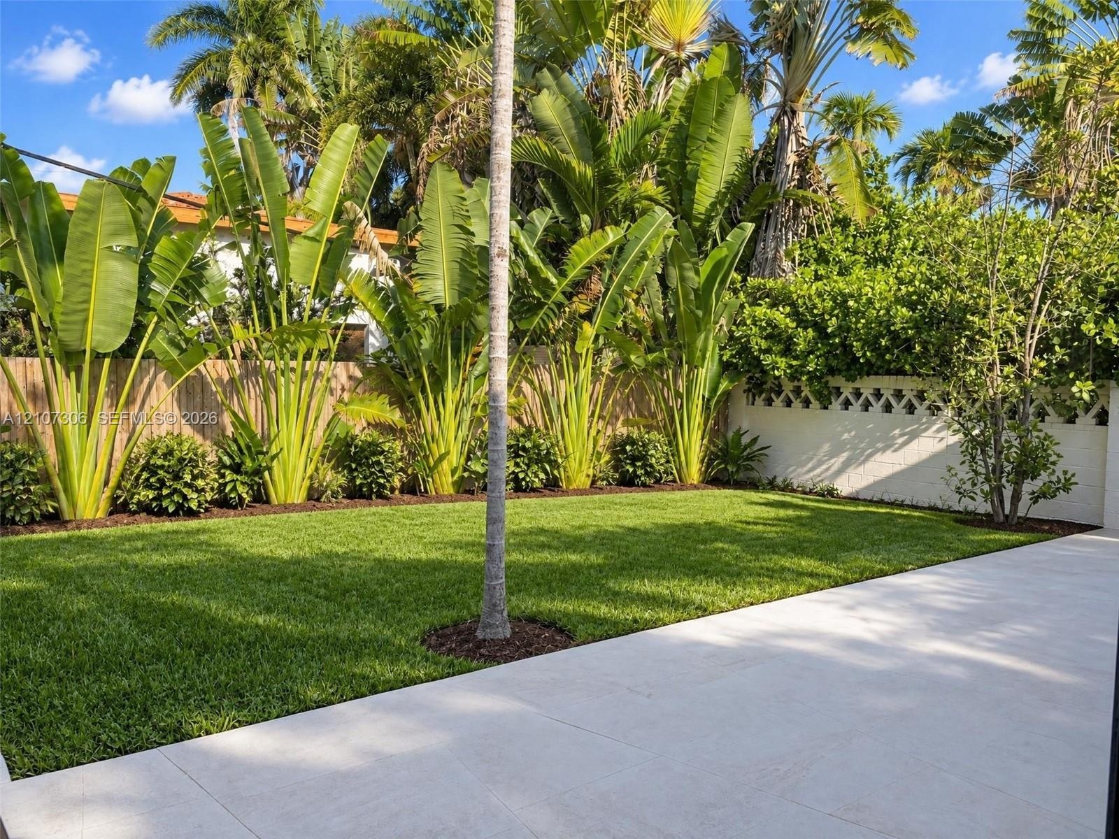 Private backyard featuring a paved stone patio, manicured lawn, established perimeter landscaping, and a decorative concrete masonry wall