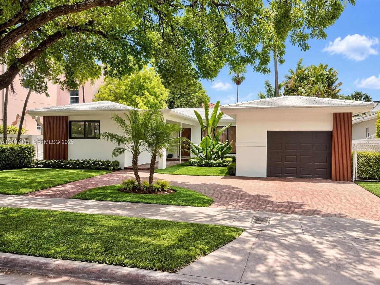 Single-story residence featuring a crisp white exterior with vertical wood-accented columns, a paved brick driveway, a dedicated garage, and mature la