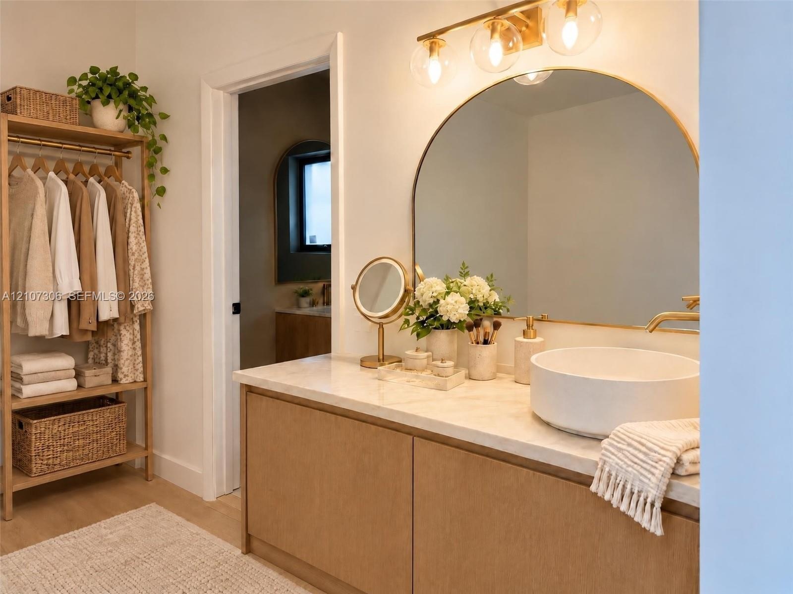 Custom wood-finish vanity with a neutral stone countertop, white vessel sink, arched wall mirror, and integrated gold-toned vanity lighting