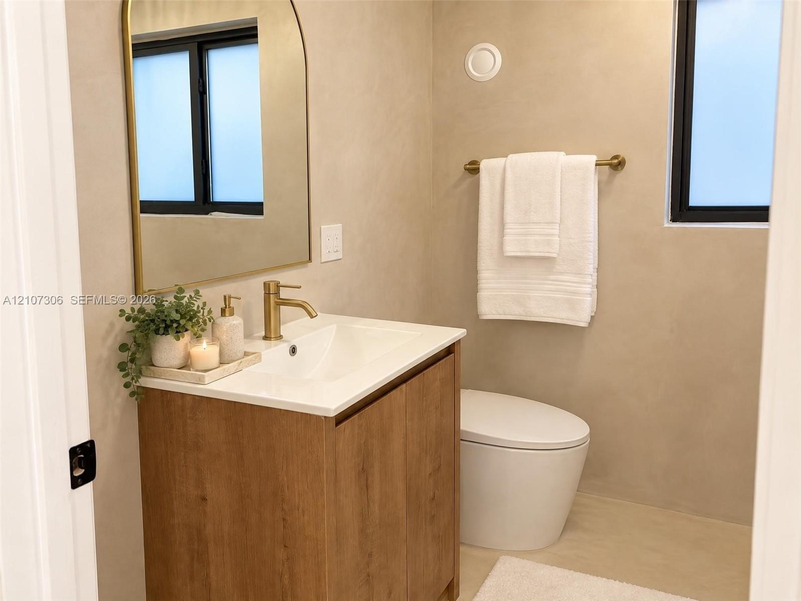 Wood-finish vanity cabinet with a white basin, arched wall mirror, brass-toned faucet, and hardware, complemented by textured wall finishes and a dual