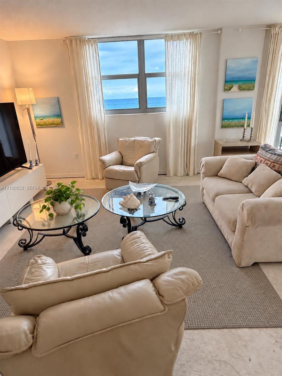 Living space featuring polished stone flooring, large picture window with ocean backdrop, and light-filled neutral interior