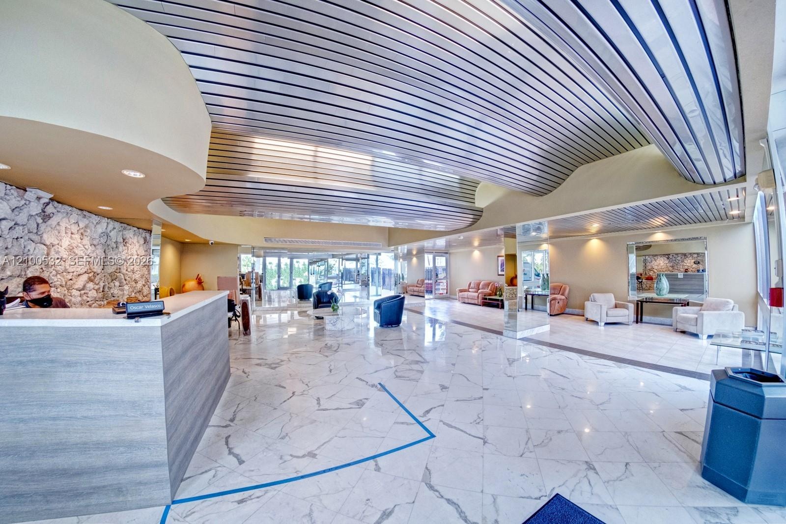 Spacious interior featuring a metallic corrugated ceiling, polished stone flooring, a large reception desk with wood-finish paneling, and an accent wa