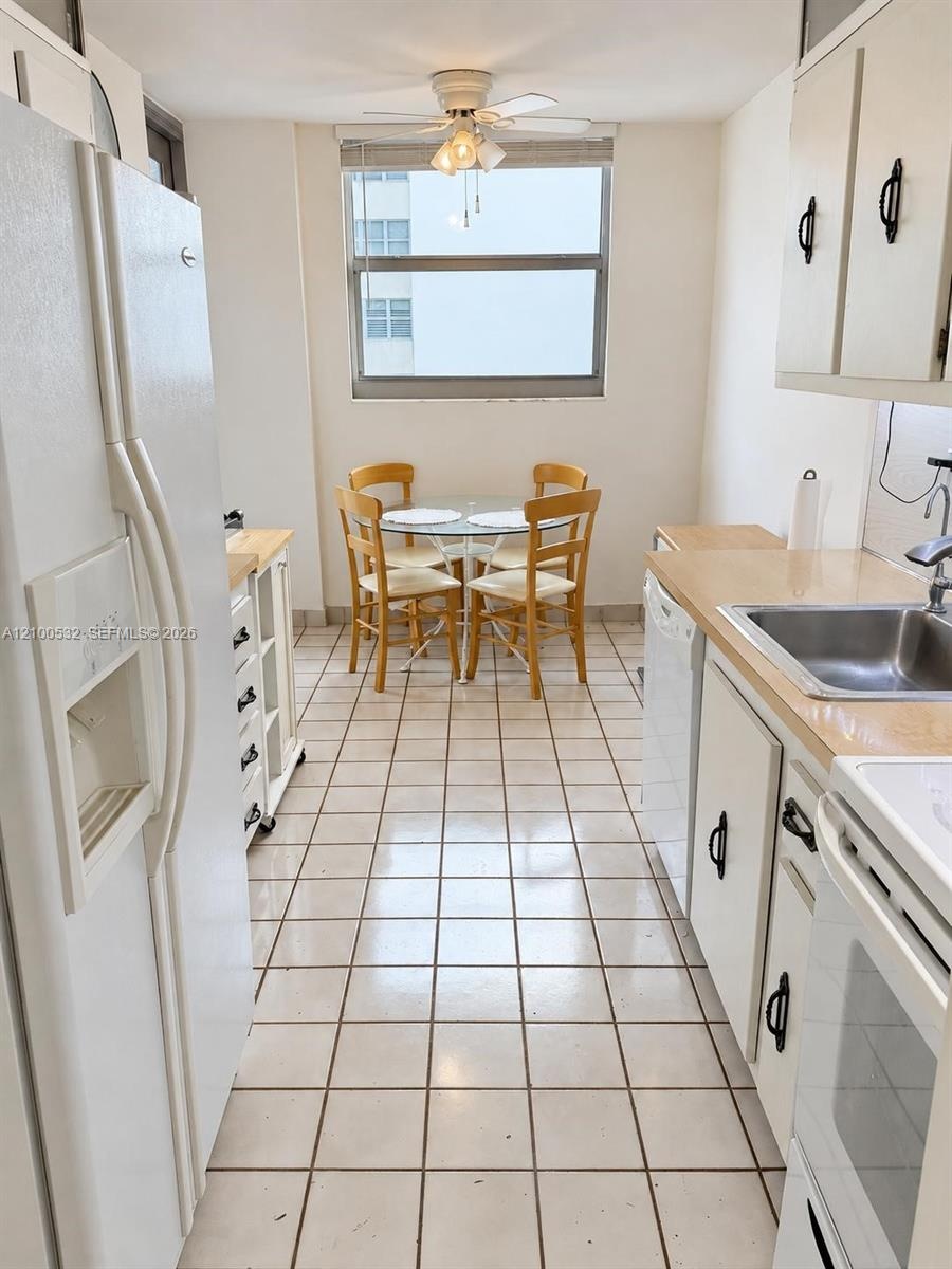 Galley kitchen featuring white cabinetry, light-toned countertops, ceramic tile flooring, a built-in stainless steel sink, and a ceiling-mounted light
