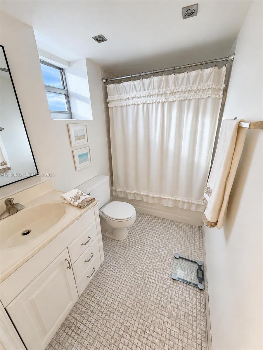 Bathroom featuring a white vanity cabinet, integrated sink with a metal faucet, mosaic tile flooring, and a tub-shower combination with recessed ceili