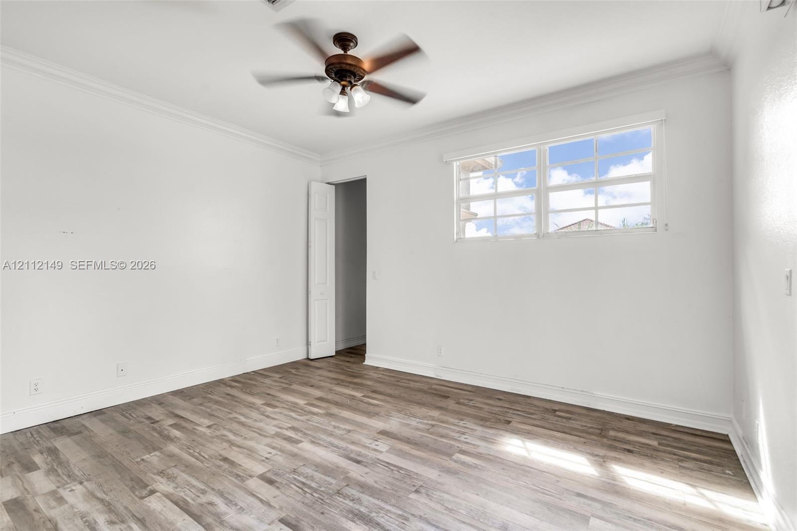 Wood-finish flooring, multi-pane window, ceiling fan with integrated lighting, and crown molding