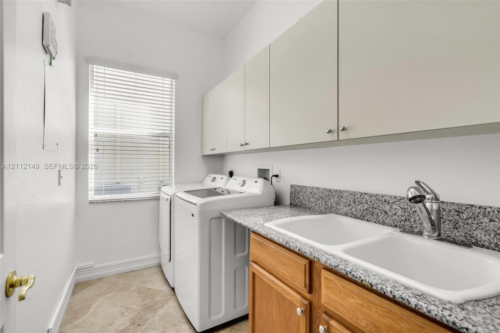 Laundry space featuring stone-composite countertop, dual-basin drop-in sink, chrome pull-down faucet, wooden base cabinetry, and overhead storage cabi