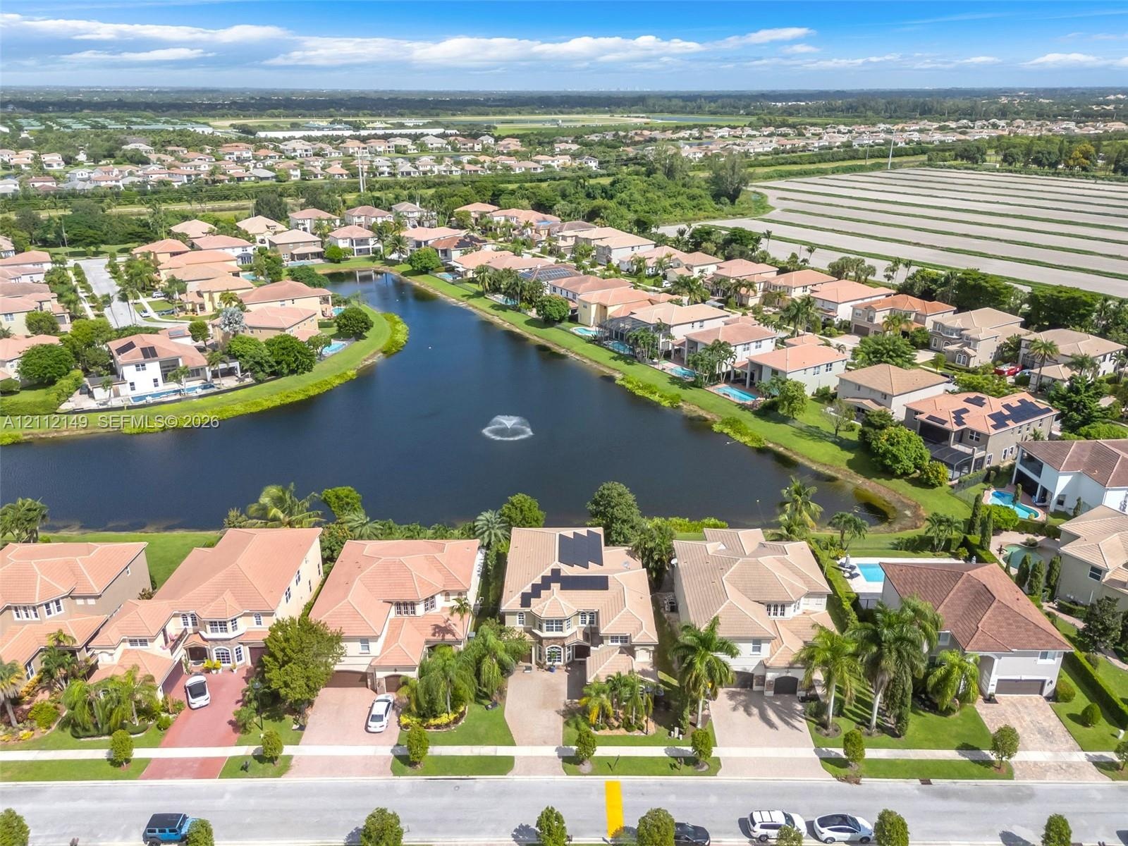 Aerial perspective of a residential community featuring multi-story homes with tile roofs, paved driveways, waterfront access to a central lake, and i