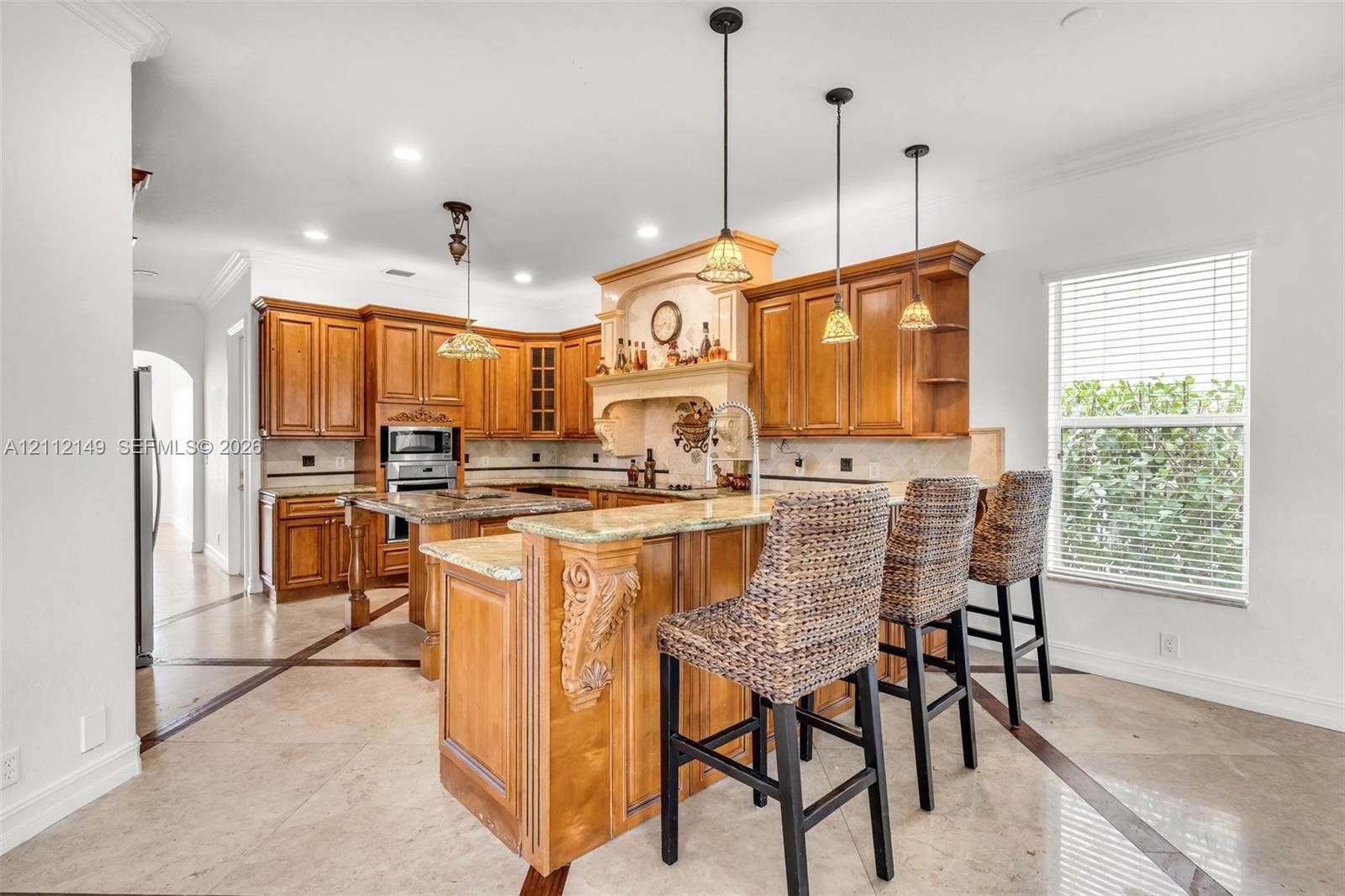 Kitchen featuring wood cabinetry, stone countertops, a tiered breakfast bar with corbel detailing, built-in stainless steel appliances, and tile floor