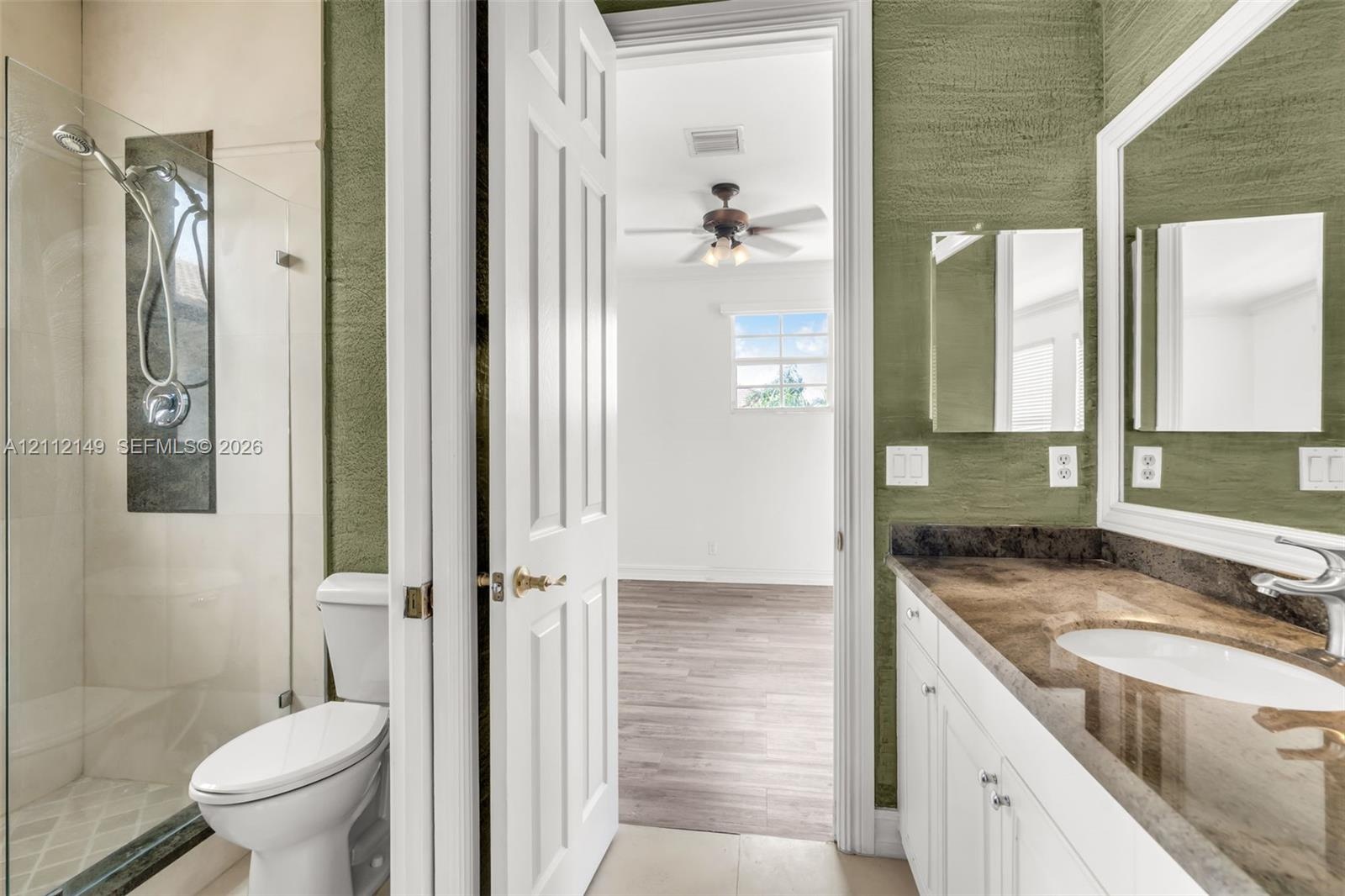 Bathroom featuring a walk-in glass-enclosed shower with metallic hardware, white cabinetry, a stone-finish countertop with an integrated basin, and te