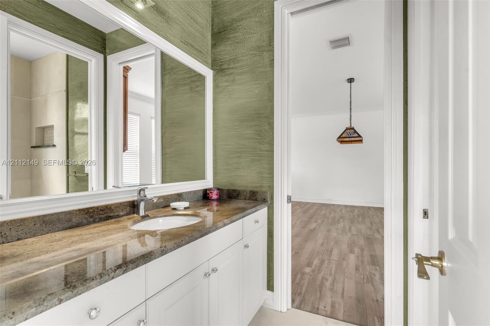 Bathroom featuring a stone-surface vanity with an integrated oval sink, white cabinetry, a full-width mirror, and textured wall treatment
