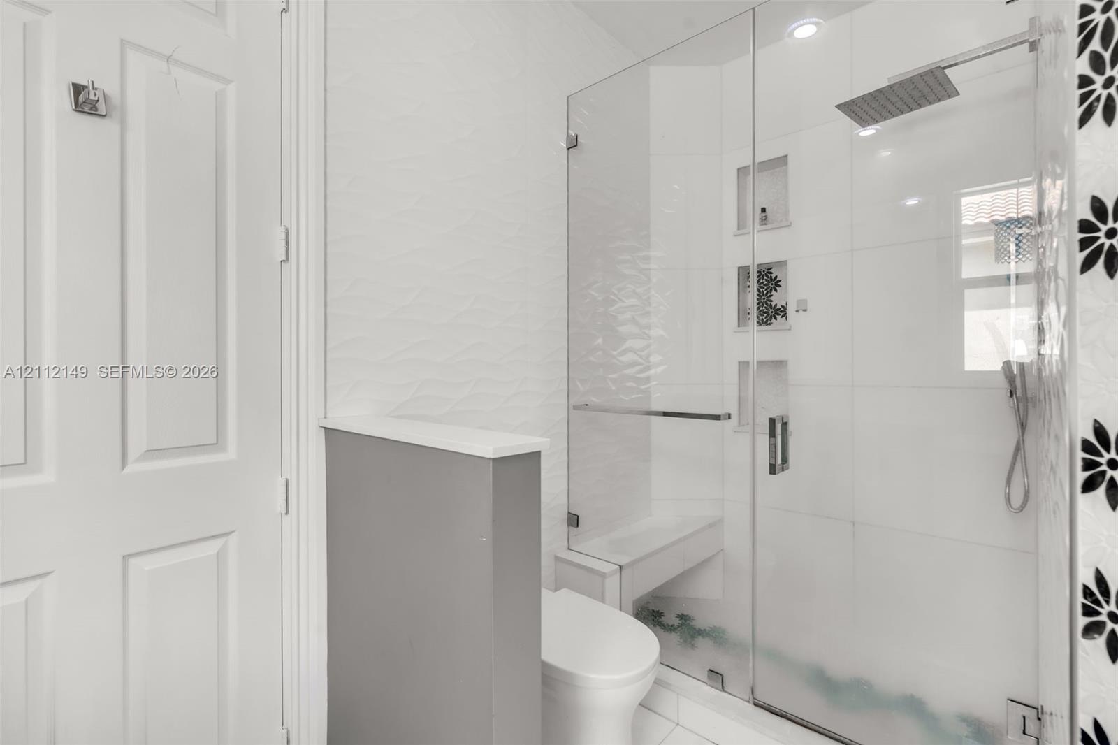 Walk-in shower featuring a glass enclosure, square rainfall shower head, handheld sprayer, built-in bench, and recessed wall niches