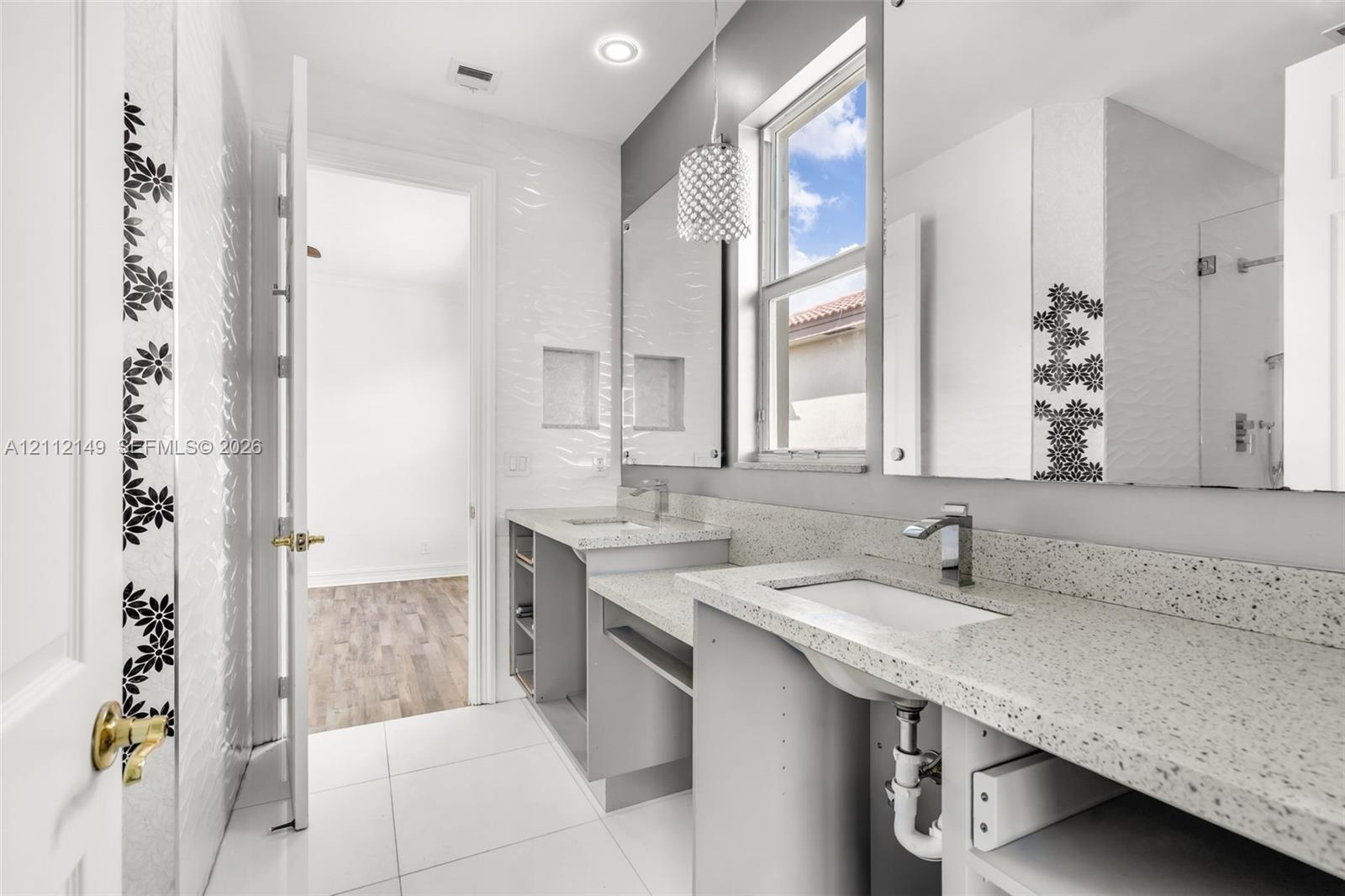 Dual-vanity bathroom featuring speckled stone-finish countertops, undermount sinks, geometric-patterned wall tile accents, and recessed wall shelving
