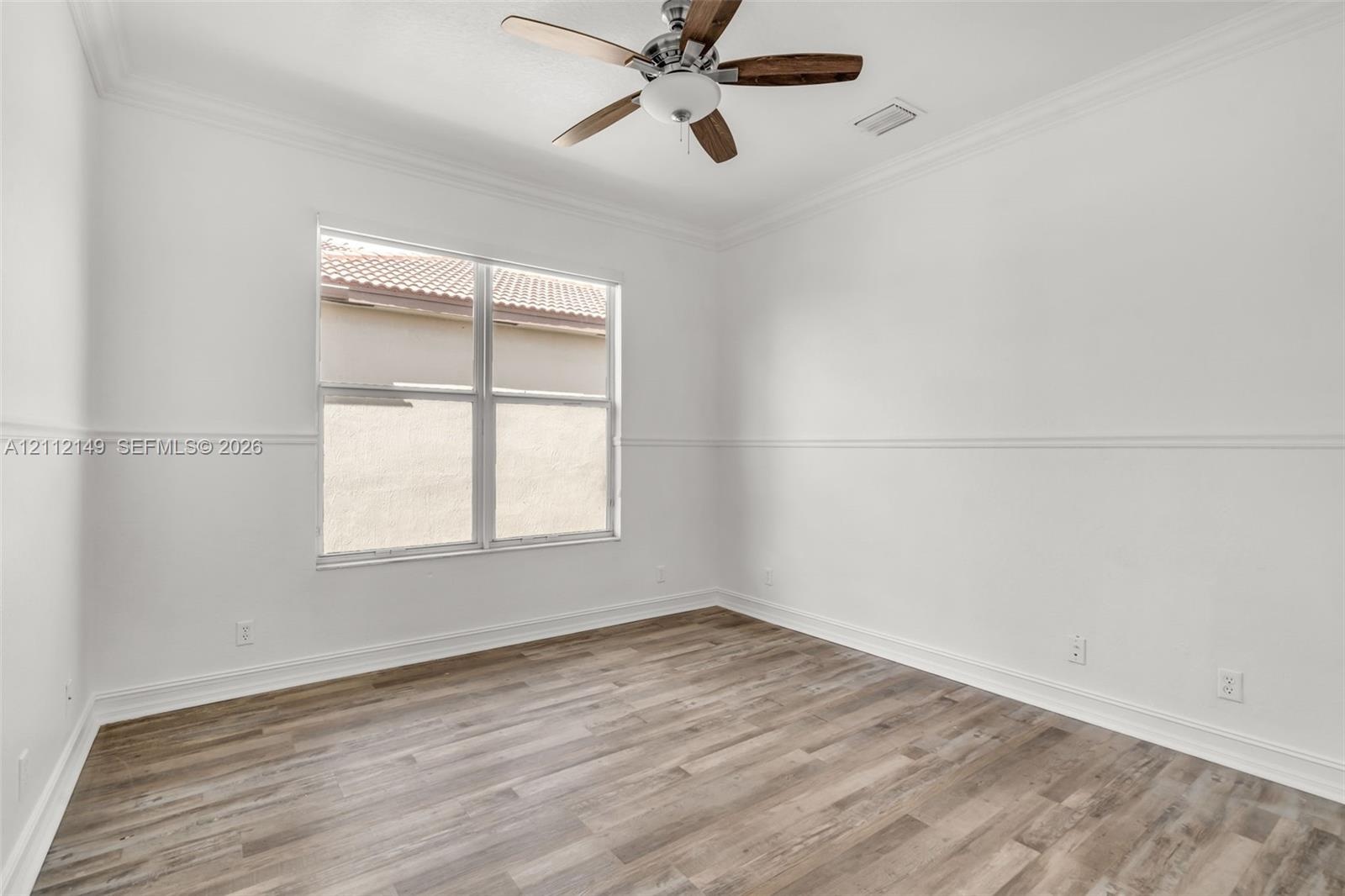 Room featuring wood-finish flooring, crown molding, chair rail trim, and a ceiling fan with integrated lighting