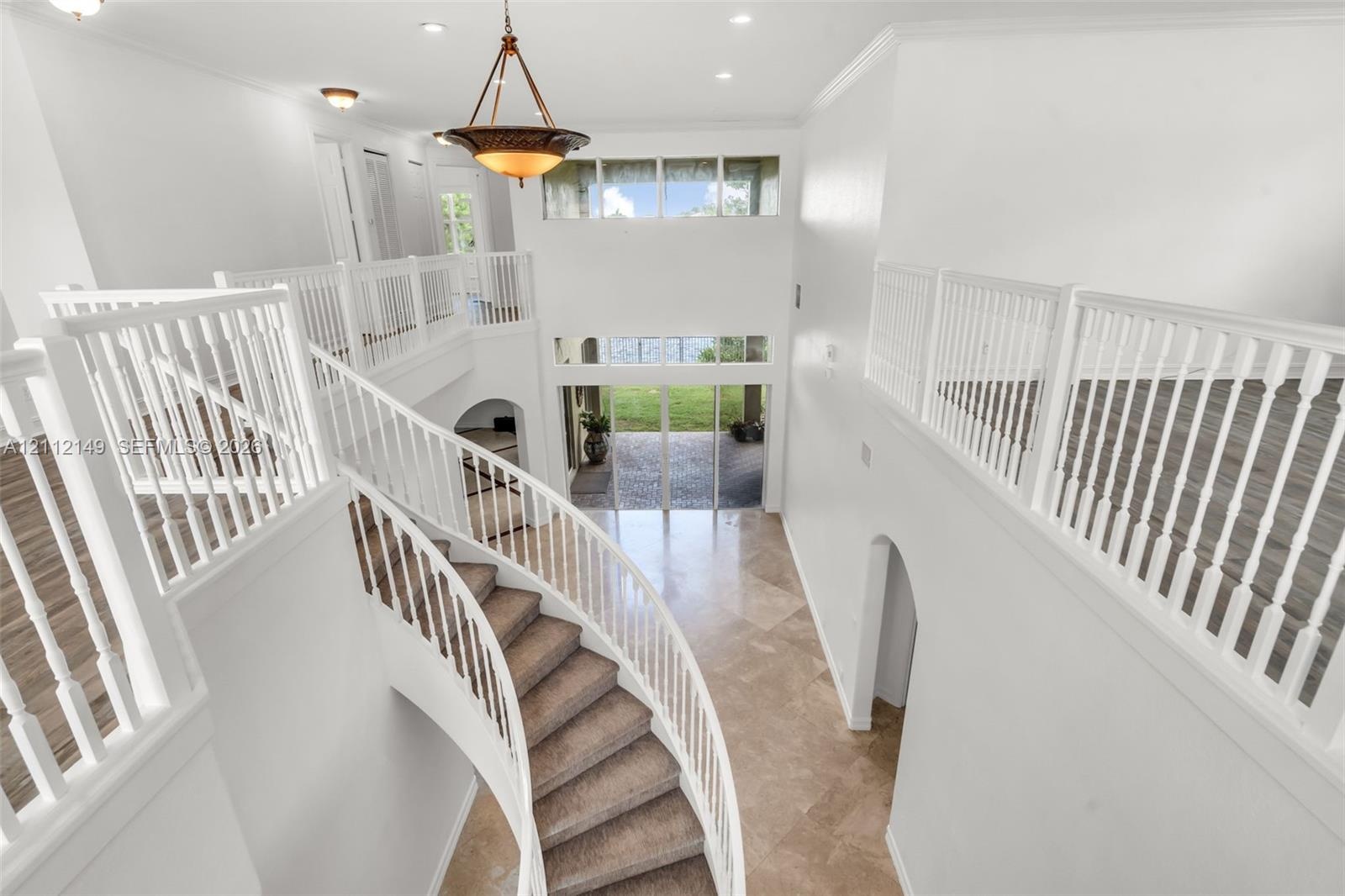Grand foyer featuring a curved staircase, stone tile flooring, multi-level ceiling heights, white wood railings, and a tiered chandelier
