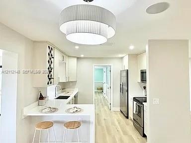 Kitchen featuring tiered pendant lighting, light wood-finish flooring, white cabinetry with built-in wine storage, stone countertops, and stainless st