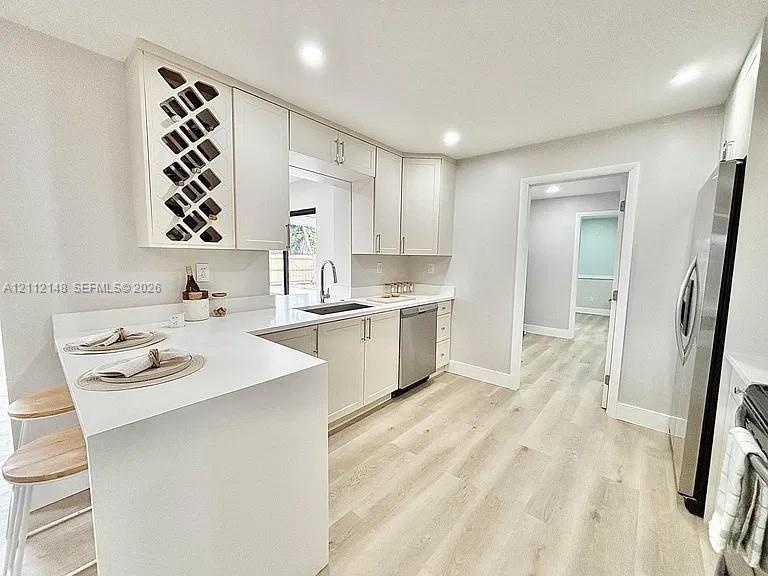 Kitchen featuring white Shaker-style cabinetry with integrated wine rack, solid-surface countertops, stainless steel appliances, and wood-finish floor