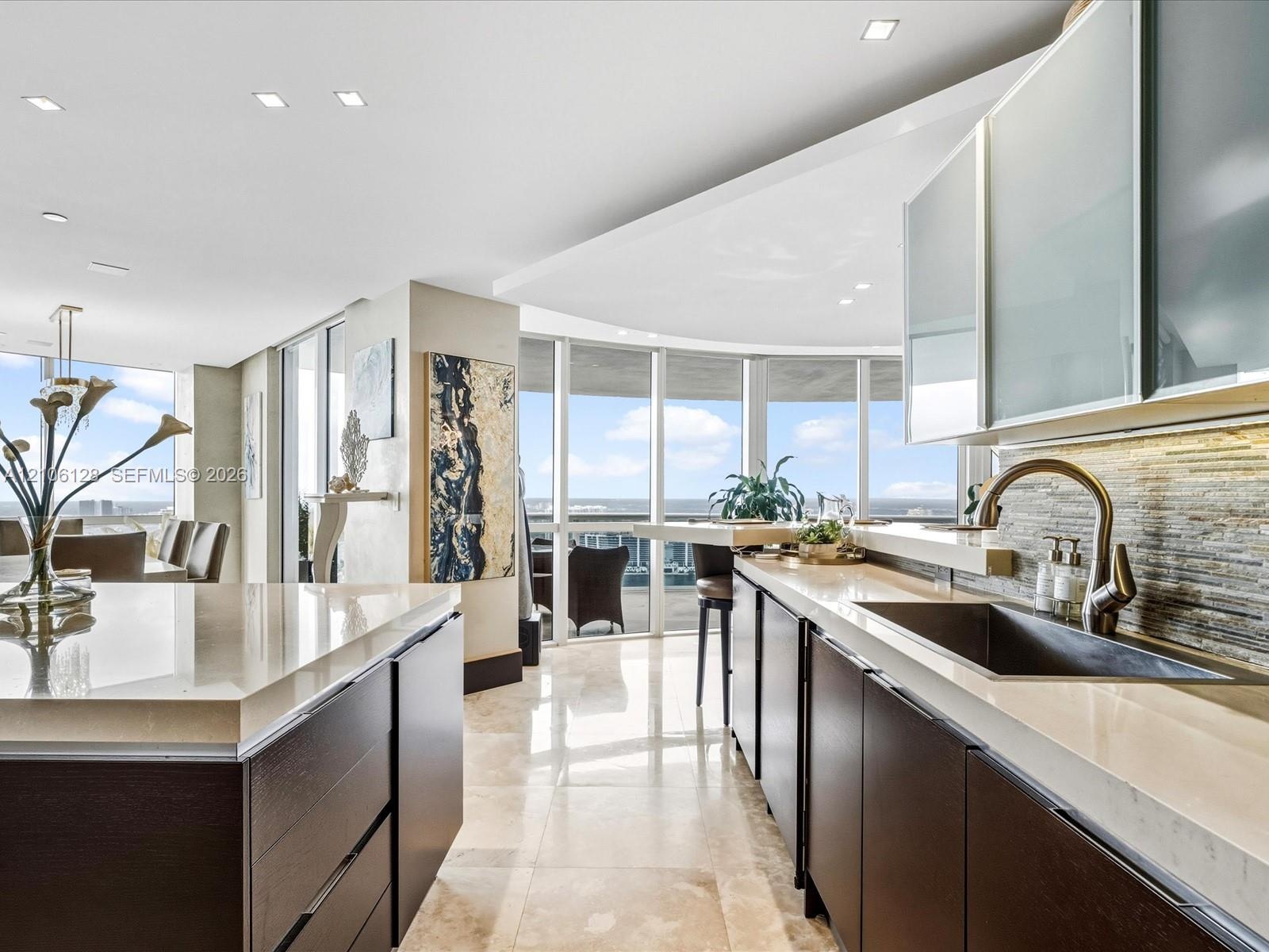 Modern kitchen featuring quartz countertops, dark wood-finish cabinetry, floor-to-ceiling windows, stacked-stone backsplash, and polished stone floori