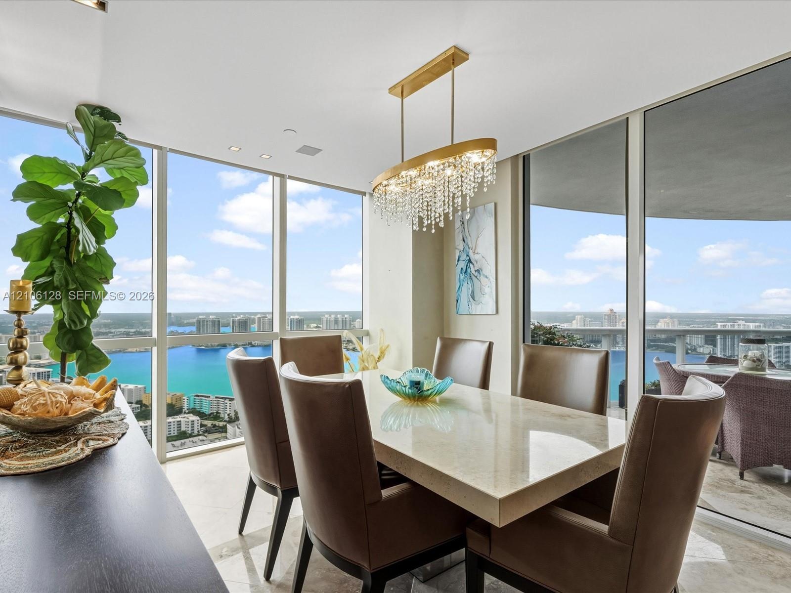 Floor-to-ceiling windows, crystal chandelier, and light-toned flooring featuring a expansive balcony and panoramic water exposure