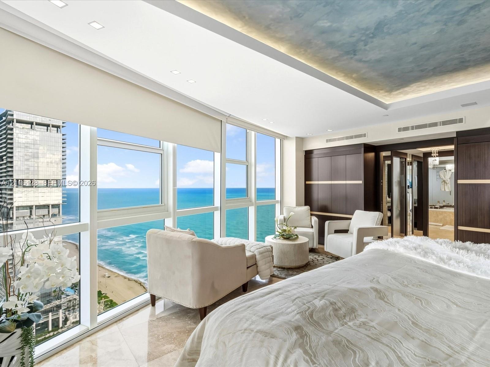 Floor-to-ceiling windows, ocean horizon backdrop, recessed ceiling lighting with painted artistic detail, built-in dark wood cabinetry, and polished s